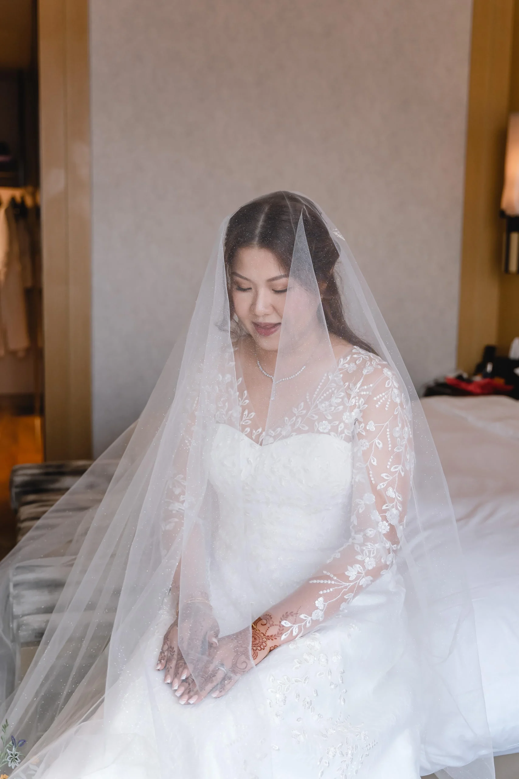 BRIDE WEARING A SEMI-BESPOKE K GOWN WEDDING DRESS WITH MULTI-FLORAL EMBROIDERED VEIL, SEATED WITH HANDS CLASPED
